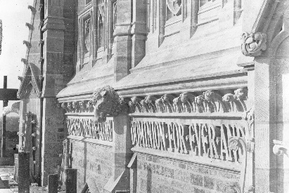 This view of the main tower, taken before the scaffolding was removed, gives dramatic point to the magnificent carving which accompanies the inscription beneath the cornice. These heads were carved in place from blocks of stone set rough-hewn. The eagles at each corner represent the Divine Providence guarding over the life of the church, and also human vigilance and insight in preserving doctrine. The four heads centered on the facades are the beasts of the Apocalypse who worshipped at the throne of the Lamb.
